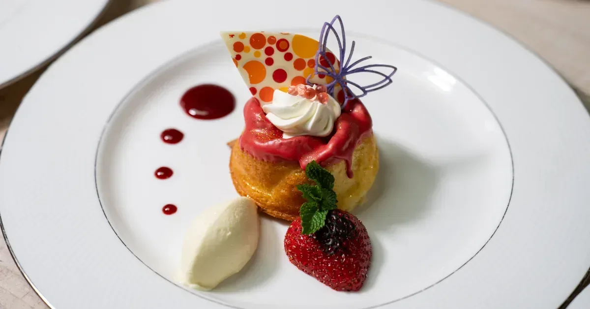 Elegant fine dining dessert plate featuring a rum baba with berry coulis, whipped cream, strawberry, vanilla ice cream, and decorative sugar art garnish.