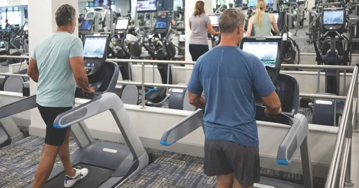 Residents enjoy modern treadmills in a spacious, well-equipped fitness center featuring rows of cardio machines and personal screens.