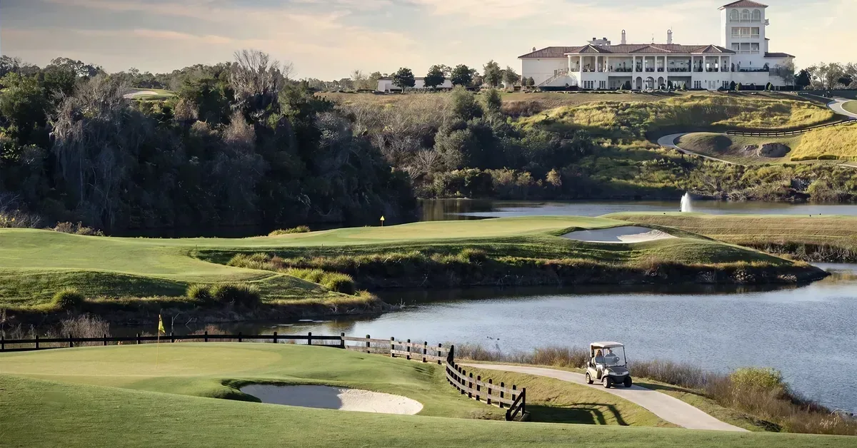 Luxury golf course community featuring manicured fairways, water features, sand bunkers, and an elegant white clubhouse perched on a scenic hillside.