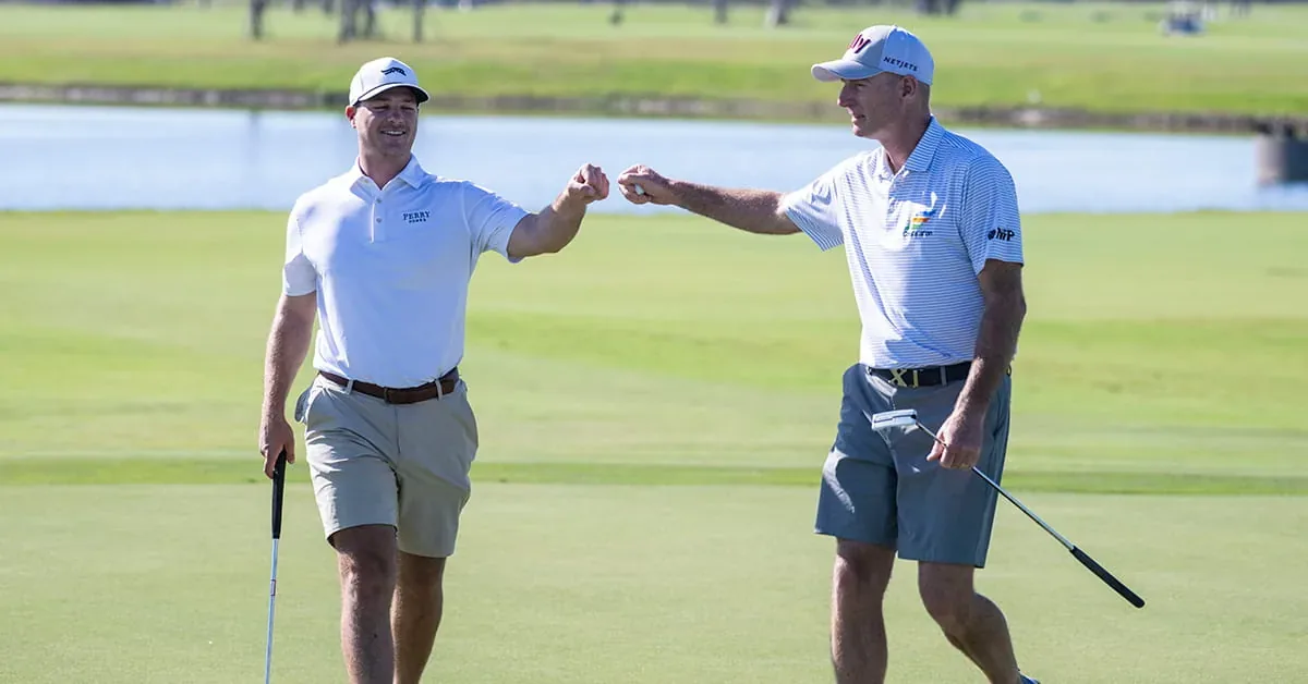 Two golfers fist bump on a lush green fairway, celebrating a successful round at a scenic golf course community.