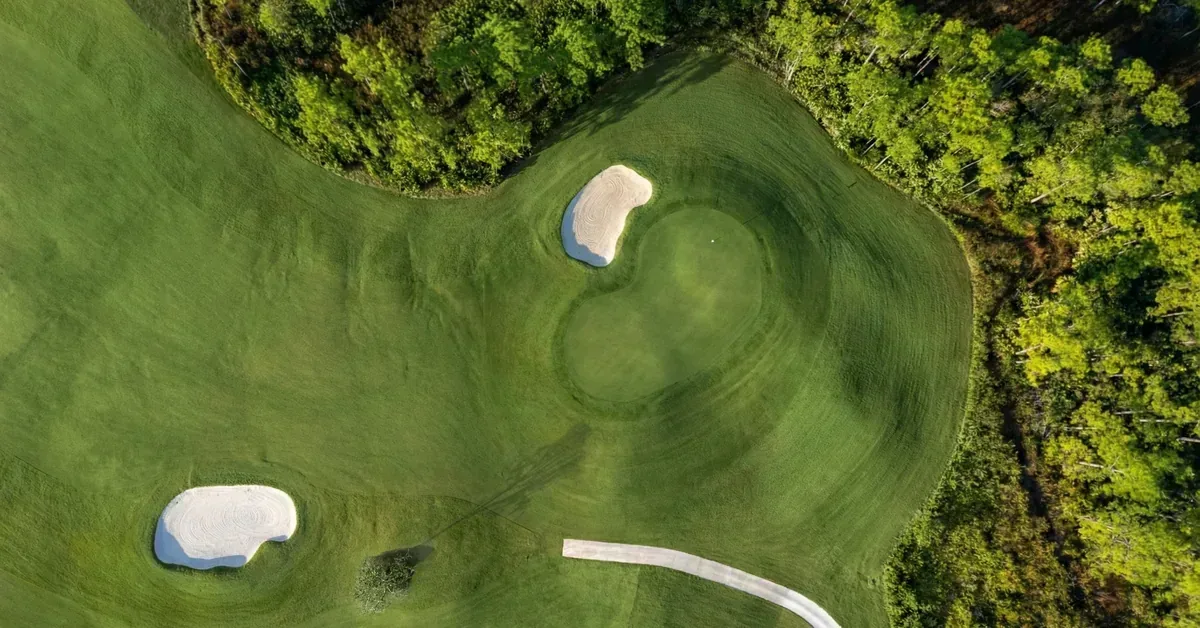 Aerial view of a pristine golf course green with sand bunkers surrounded by lush trees, showcasing luxury resort-style amenities.