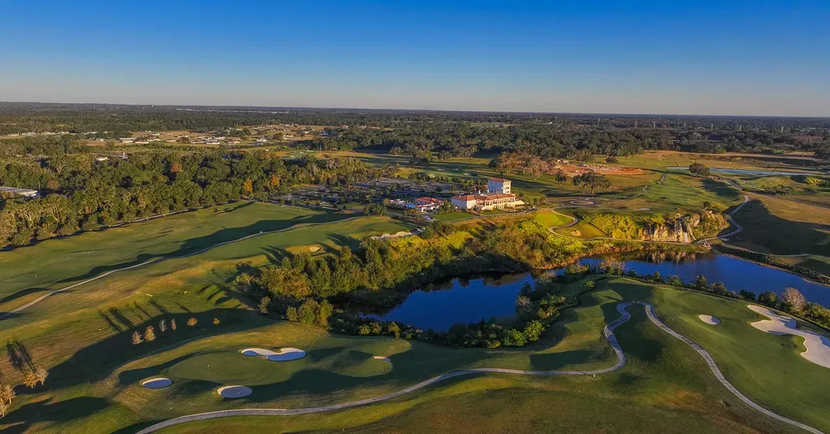 Aerial view of a championship golf course featuring manicured fairways, sand bunkers, serene water hazards, and an elegant clubhouse surrounded by lush Flori...
