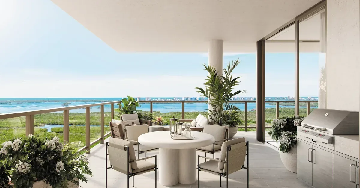 Luxury waterfront balcony with outdoor dining set, built-in grill, and sweeping ocean views framed by lush tropical greenery.