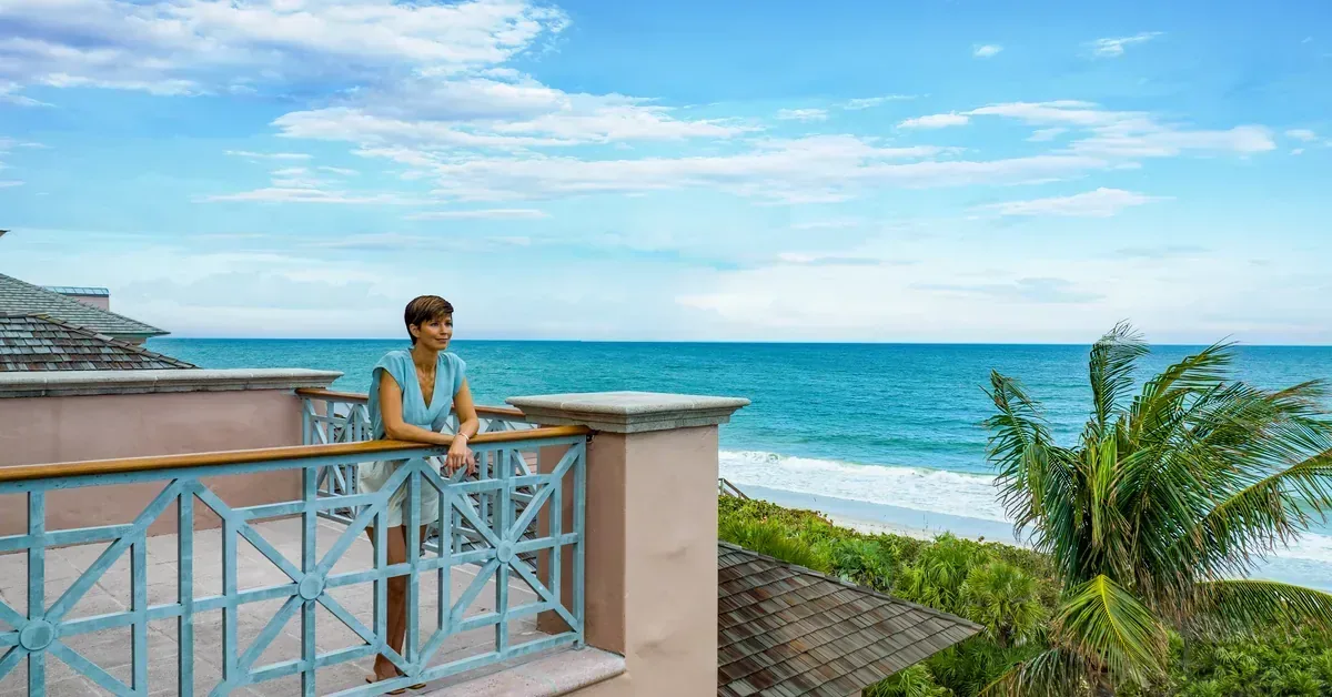 A woman relaxes on an elegant oceanfront balcony, enjoying breathtaking turquoise water views at a luxury beachfront property.
