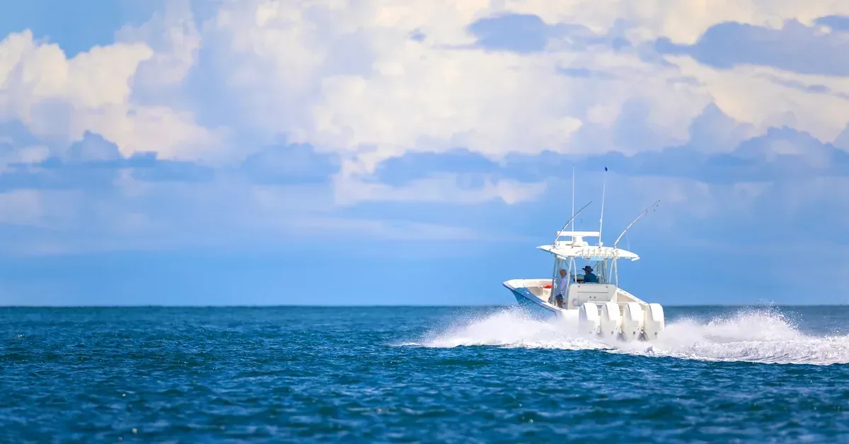 A white center console fishing boat speeds across blue ocean waters beneath a dramatic cloudy sky, perfect for coastal lifestyle enthusiasts.